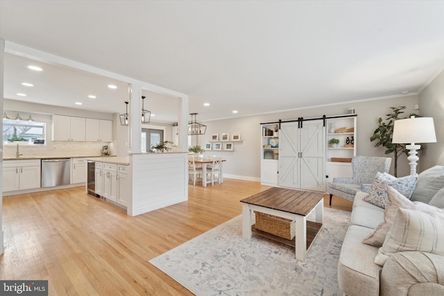 living room featuring sink, beverage cooler, crown molding, a barn door, and light hardwood / wood-style flooring