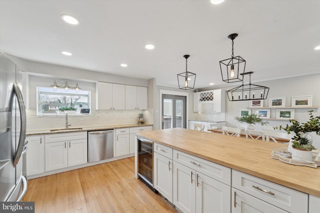 kitchen featuring wine cooler, sink, white cabinetry, appliances with stainless steel finishes, and pendant lighting