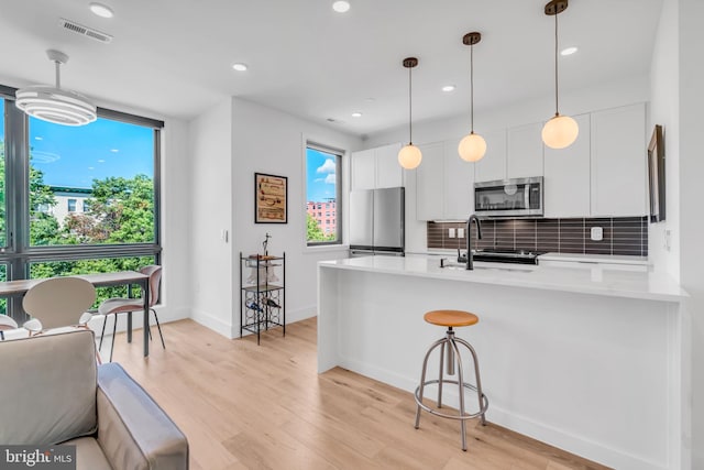 kitchen with appliances with stainless steel finishes, white cabinetry, decorative backsplash, light hardwood / wood-style floors, and kitchen peninsula