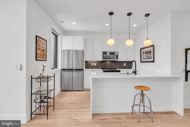 kitchen with sink, appliances with stainless steel finishes, white cabinetry, kitchen peninsula, and light wood-type flooring