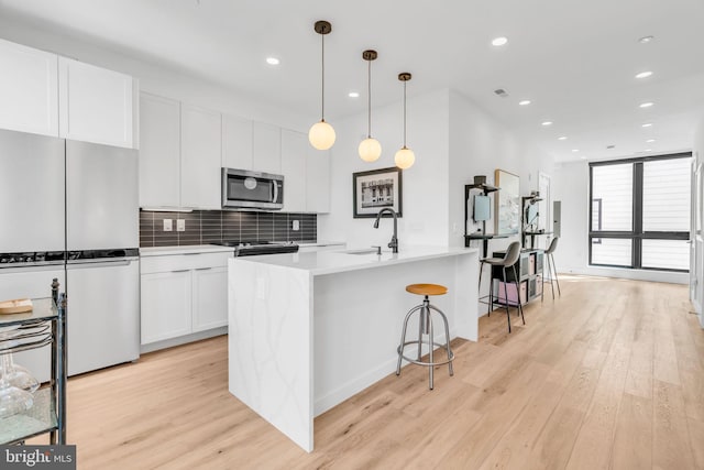 kitchen featuring decorative light fixtures, an island with sink, white cabinets, decorative backsplash, and fridge