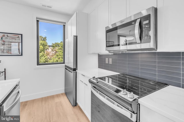 kitchen with appliances with stainless steel finishes, tasteful backsplash, light stone countertops, white cabinets, and light wood-type flooring