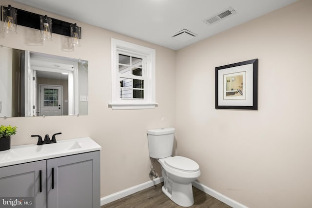 half bath with toilet, wood finished floors, vanity, visible vents, and baseboards