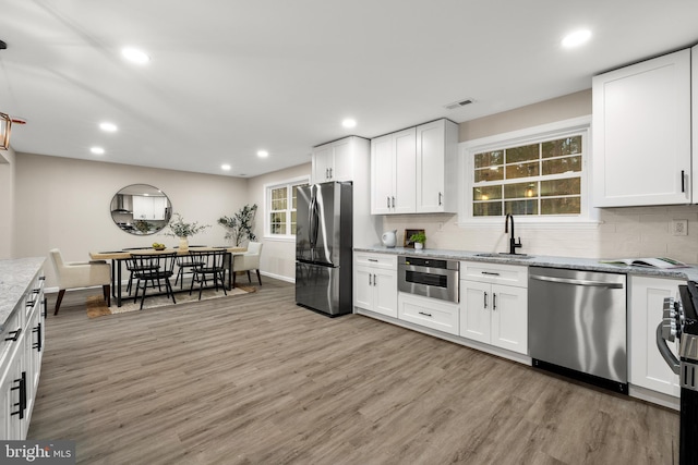 kitchen with tasteful backsplash, light stone counters, stainless steel appliances, light wood-type flooring, and a sink