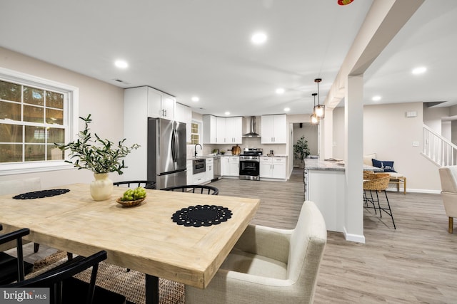 kitchen featuring stainless steel appliances, light wood-type flooring, white cabinetry, and wall chimney exhaust hood