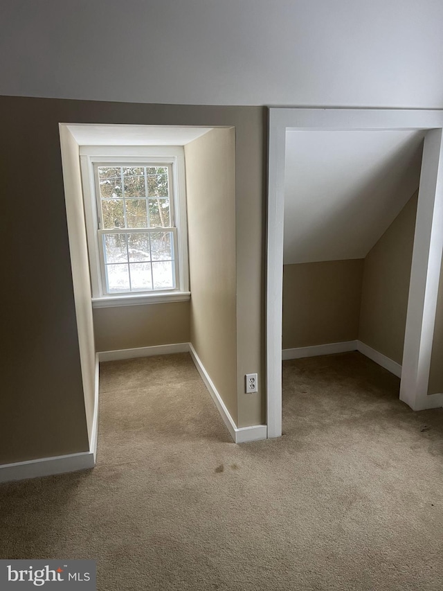 additional living space featuring baseboards, vaulted ceiling, and light colored carpet