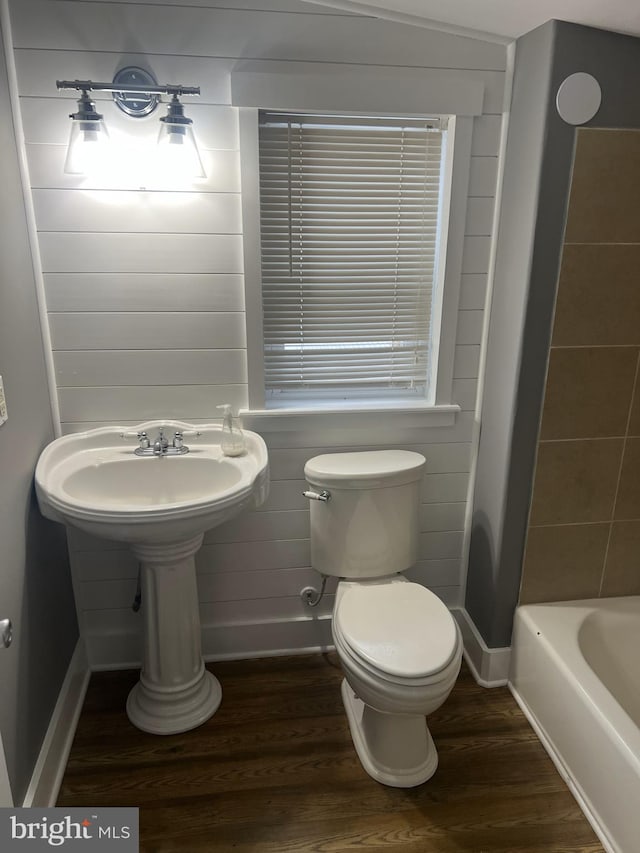 bathroom featuring a bath, baseboards, toilet, and wood finished floors