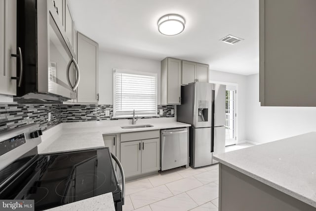 kitchen featuring appliances with stainless steel finishes, gray cabinets, sink, and decorative backsplash