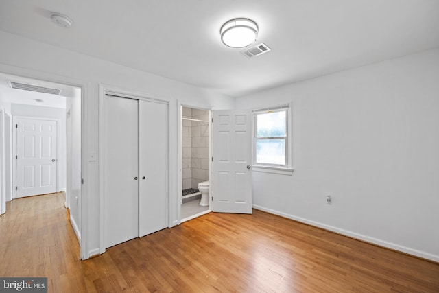 unfurnished bedroom with ensuite bath, a closet, and light wood-type flooring