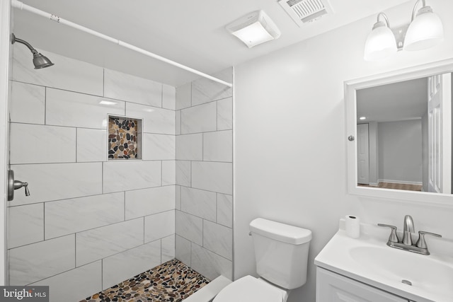 bathroom with vanity, a tile shower, and toilet