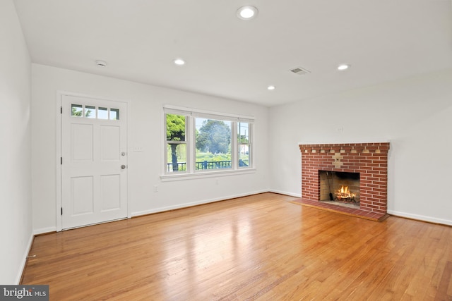 unfurnished living room with a brick fireplace and light hardwood / wood-style flooring