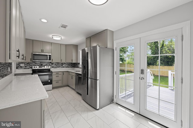 kitchen featuring french doors, gray cabinetry, light stone counters, appliances with stainless steel finishes, and decorative backsplash