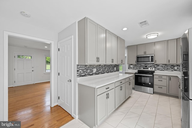 kitchen with gray cabinets, tasteful backsplash, appliances with stainless steel finishes, and light hardwood / wood-style flooring