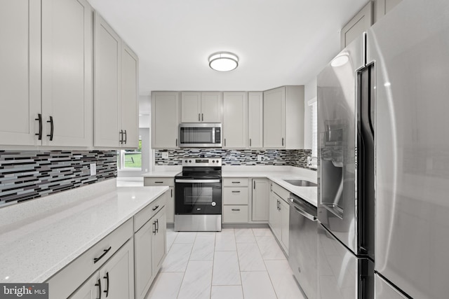 kitchen with gray cabinets, appliances with stainless steel finishes, sink, decorative backsplash, and light stone countertops