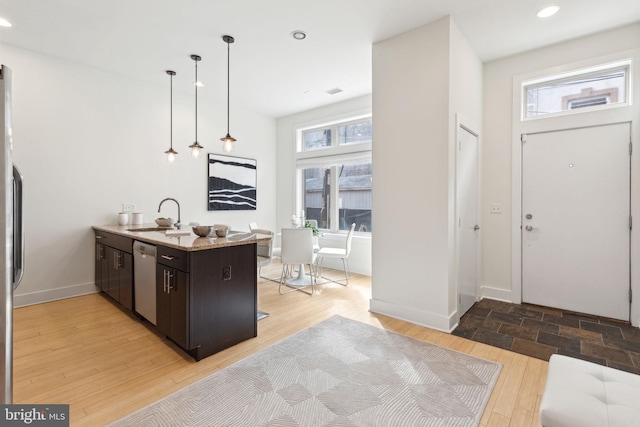 kitchen featuring a sink, dark brown cabinets, stainless steel dishwasher, hanging light fixtures, and light wood-type flooring