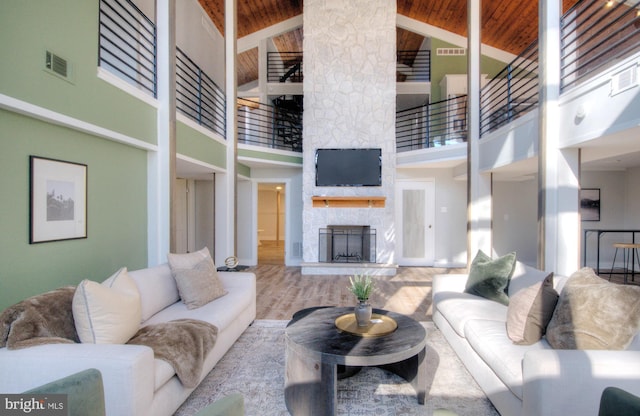 living room with a high ceiling, a fireplace, light hardwood / wood-style floors, wooden ceiling, and beamed ceiling