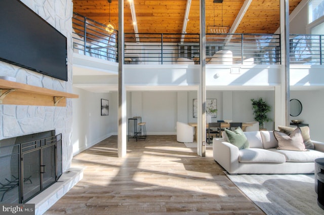 living room featuring a high ceiling, wood-type flooring, a stone fireplace, and wood ceiling