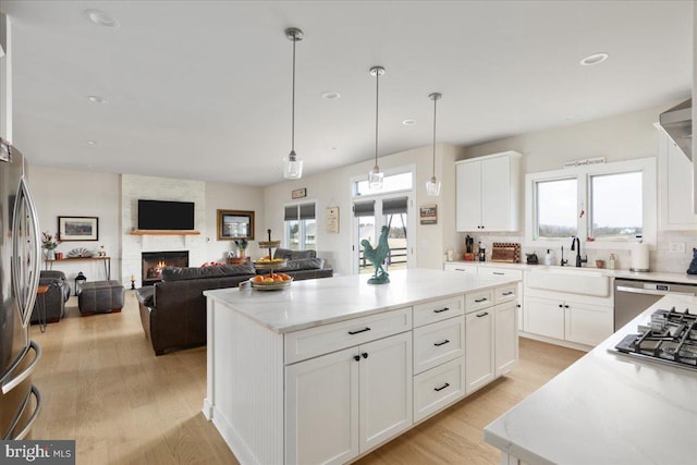 kitchen featuring stainless steel appliances, a fireplace, a sink, a center island, and light wood finished floors