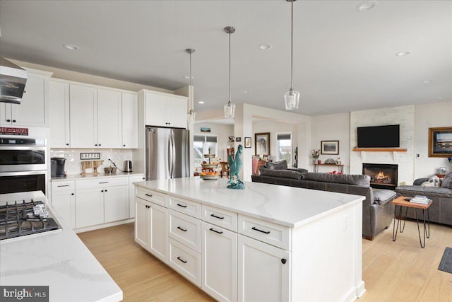 kitchen with stainless steel appliances, hanging light fixtures, light wood-style flooring, and white cabinetry