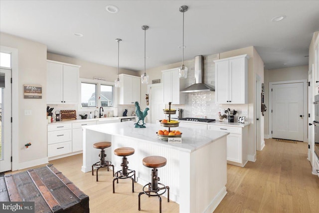 kitchen with a breakfast bar area, light wood finished floors, white cabinets, a kitchen island, and wall chimney exhaust hood