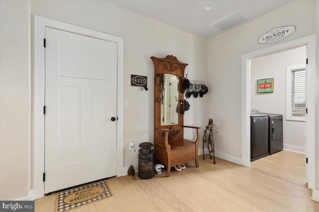 foyer entrance featuring light wood-style flooring, washing machine and dryer, visible vents, and baseboards