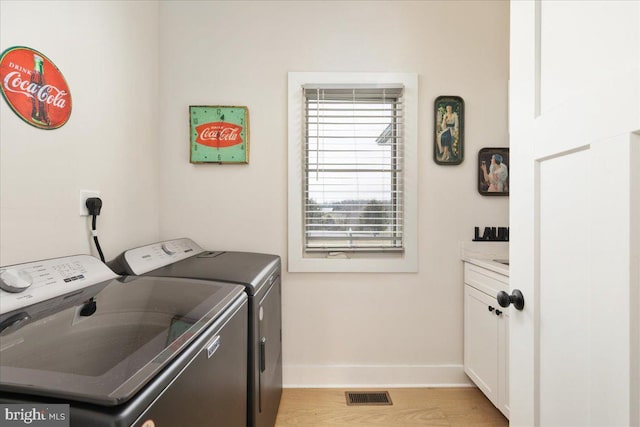 washroom featuring light wood-style flooring, separate washer and dryer, visible vents, baseboards, and cabinet space