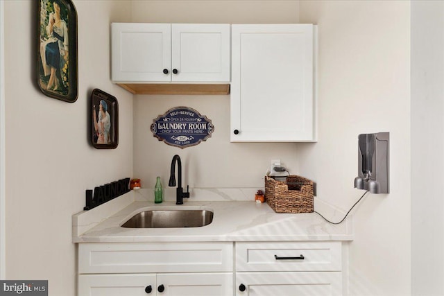 kitchen with a sink, white cabinetry, and light stone countertops