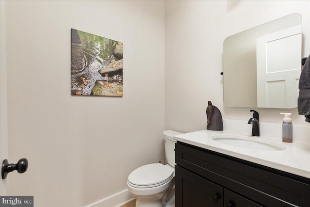 half bath featuring baseboards, vanity, and toilet