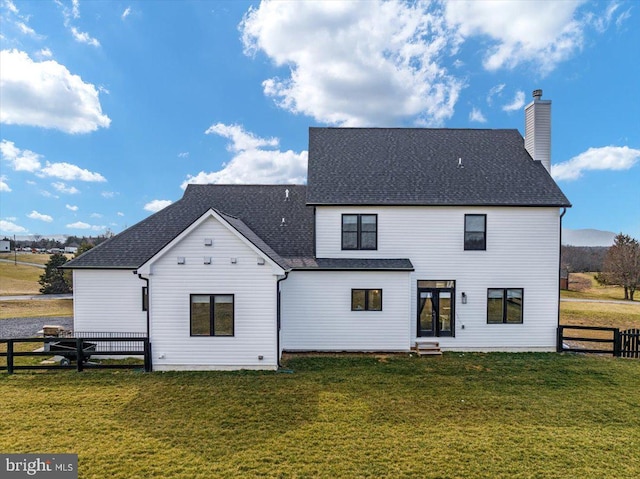 back of house featuring roof with shingles, a lawn, a chimney, and fence