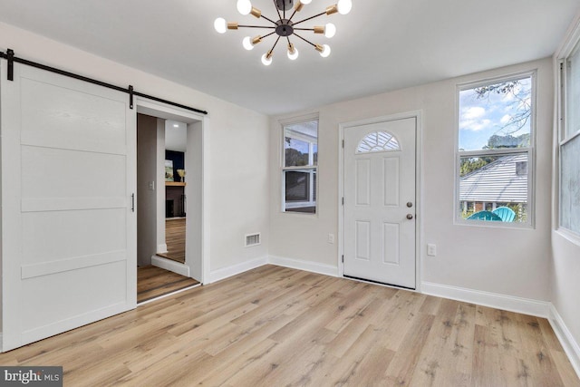 foyer entrance featuring a notable chandelier, a barn door, and light wood-type flooring