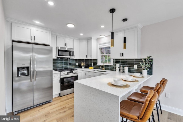 kitchen featuring appliances with stainless steel finishes, sink, white cabinets, hanging light fixtures, and kitchen peninsula