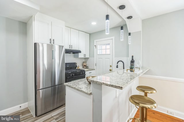 kitchen with black gas range oven, stainless steel refrigerator, white cabinetry, kitchen peninsula, and light stone countertops