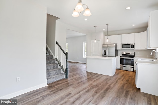 kitchen with a kitchen island, appliances with stainless steel finishes, pendant lighting, white cabinetry, and sink