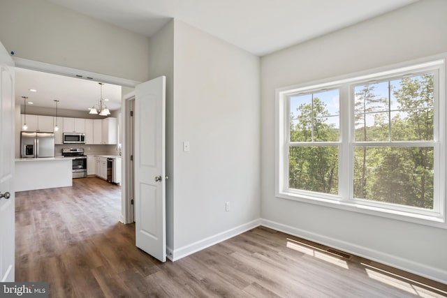 unfurnished room featuring wood-type flooring, plenty of natural light, and an inviting chandelier