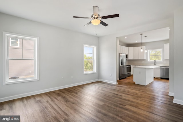 kitchen with a center island, hanging light fixtures, appliances with stainless steel finishes, hardwood / wood-style flooring, and white cabinets