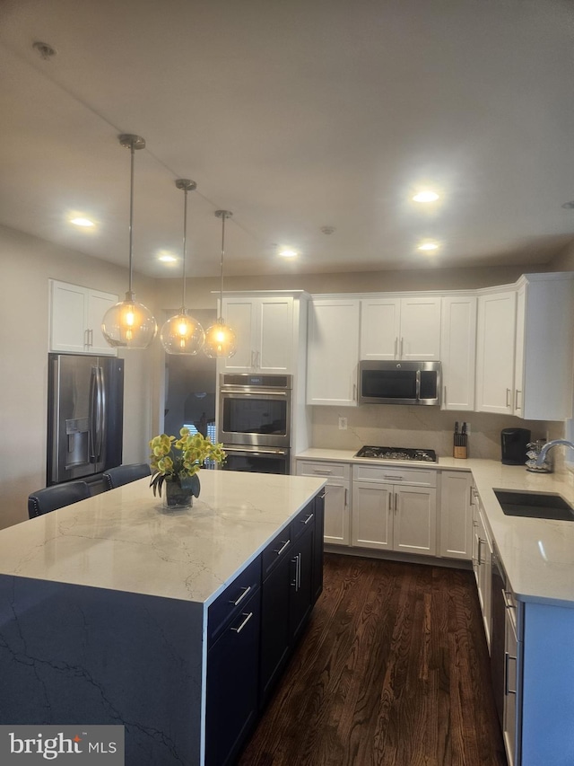 kitchen featuring sink, appliances with stainless steel finishes, white cabinets, a kitchen island, and decorative light fixtures