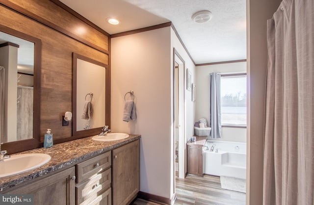 bathroom featuring wood-type flooring, vanity, a washtub, crown molding, and a textured ceiling