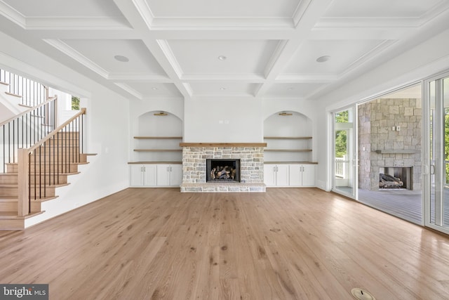 unfurnished living room with built in features, light wood-style floors, and a stone fireplace