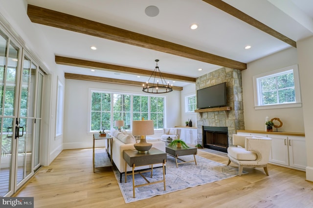 living area featuring light wood-type flooring, a stone fireplace, a notable chandelier, and a wealth of natural light