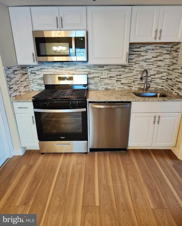 kitchen with appliances with stainless steel finishes, light stone countertops, light hardwood / wood-style flooring, and white cabinets