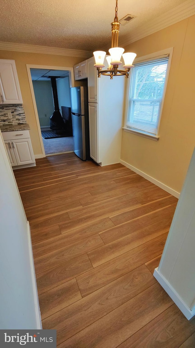 kitchen with white cabinetry, decorative light fixtures, light hardwood / wood-style floors, and stainless steel refrigerator