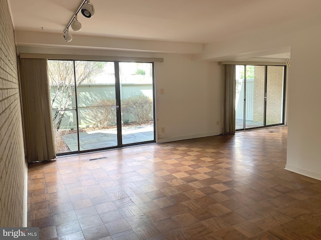 empty room featuring visible vents, rail lighting, and baseboards