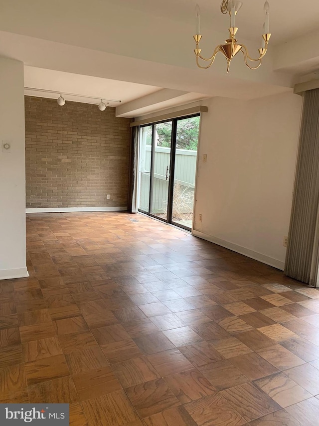 empty room with an inviting chandelier, brick wall, and baseboards