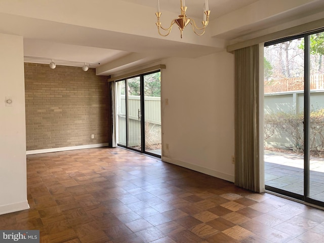 spare room featuring baseboards, brick wall, track lighting, and a notable chandelier