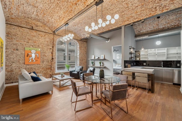 dining area featuring hardwood / wood-style flooring, brick ceiling, brick wall, and a towering ceiling