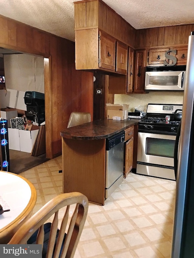 kitchen with appliances with stainless steel finishes, a textured ceiling, wooden walls, and kitchen peninsula