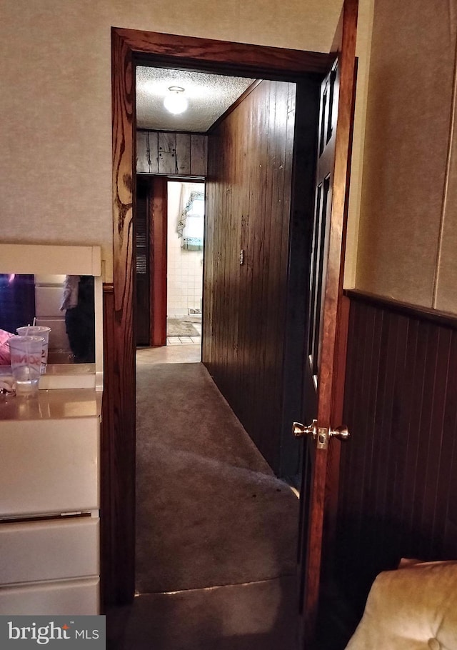 hallway featuring carpet floors, a textured ceiling, and wood walls