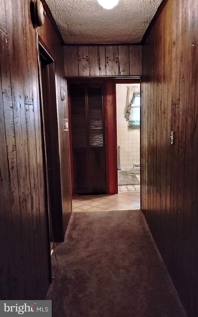 hall with wooden walls, light colored carpet, and a textured ceiling