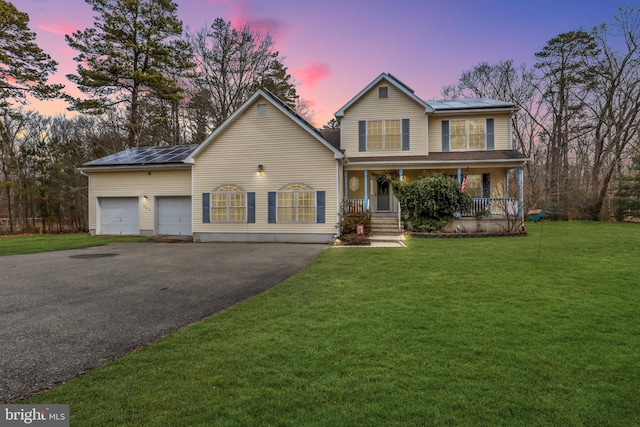 view of front of house with driveway, a porch, a front yard, and roof mounted solar panels