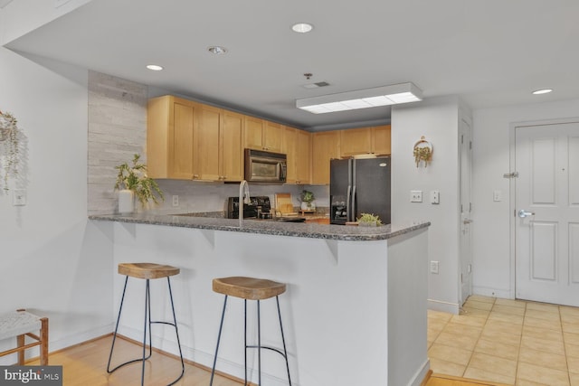 kitchen with black appliances, a breakfast bar area, a peninsula, recessed lighting, and baseboards